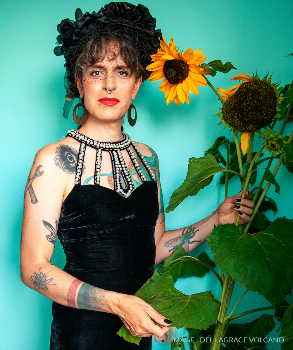 Zafira Vrba Woodski in a black dress with sunflowers and a teal background